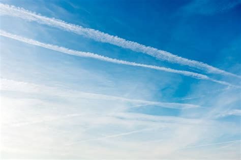 Blue sky with several white linear cloud trails, including two thicker parallel trails across the upper half and thinner spreading lines below